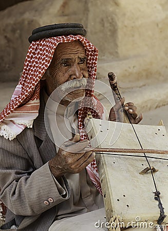 Little Petra, Jordan â€“ June 20, 2017: Old Bedouin man or Arab man in traditional outfit, playing his musical instrument . Editorial Stock Photo